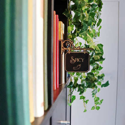 Booktrovert-Schild mit goldener Spicy Gravur in einem Bücherregal mit Efeu